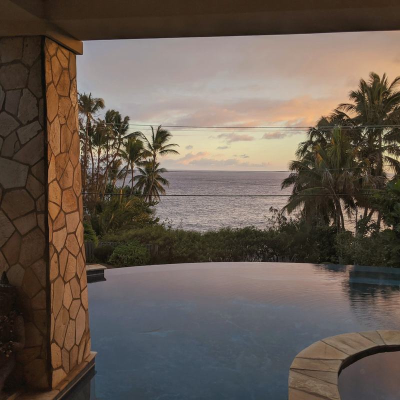 Infinity-Pool zwischen Steinsäulen mit Blick auf Palmen und Meer bei Sonnenuntergang